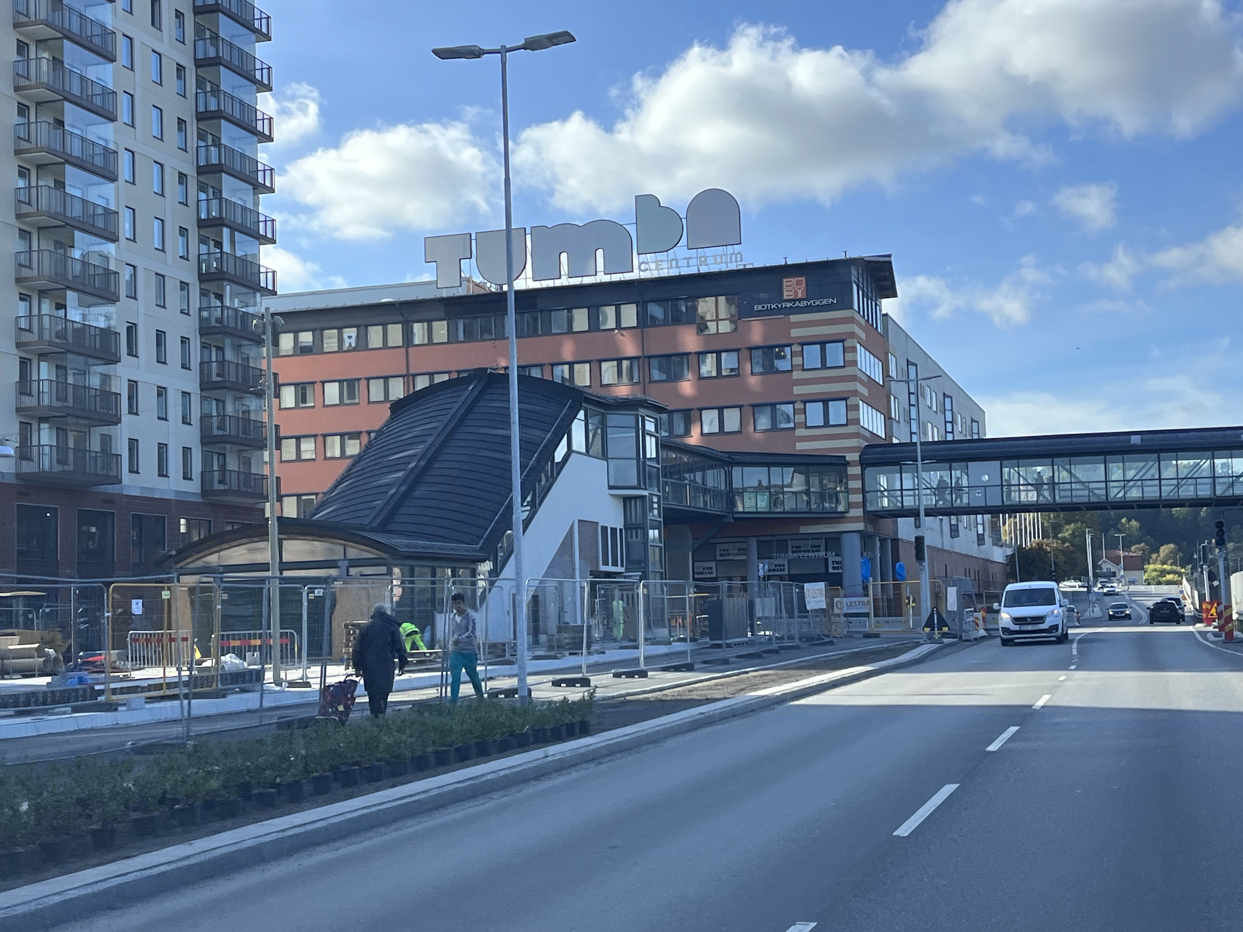 Pågående bygg- och vägarbeten i Tumba centrum med nybyggda bostadshus och stationsområde i bakgrunden.